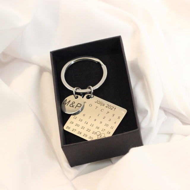Atslēgu piekariņš ar kalendāra gravējumu sudraba krāsā un papildus mazo medaljonu.